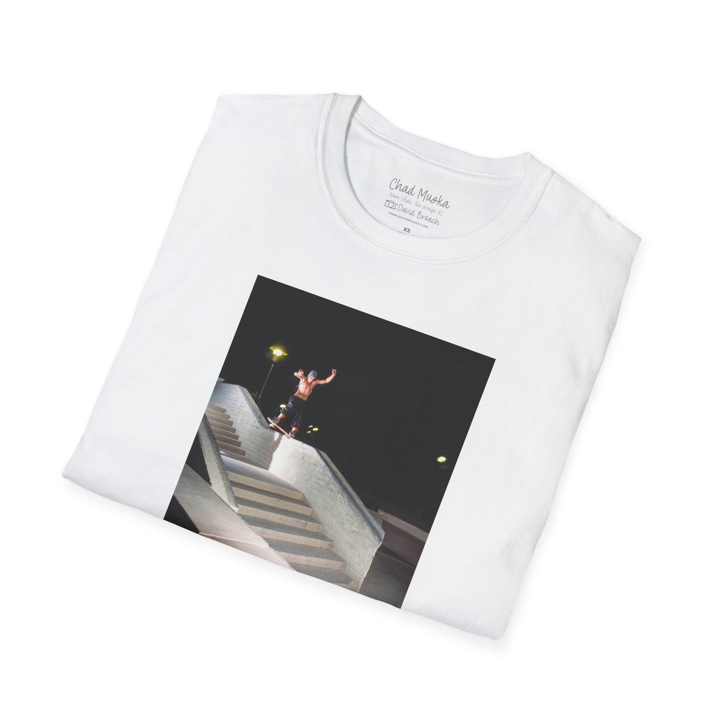 A neatly folded white crew neck short-sleeve T-shirt featuring a printed photo of A high-quality print featuring an iconic shot of Chad Muska in 1999 executing a smooth nose slide down the triple-kink Hubba rail at The Wedge in Phoenix, Arizona. Captured by photographer David Broach, this image showcases Muska’s signature style and fearless approach, making it a must-have for skateboarding enthusiasts and collectors."