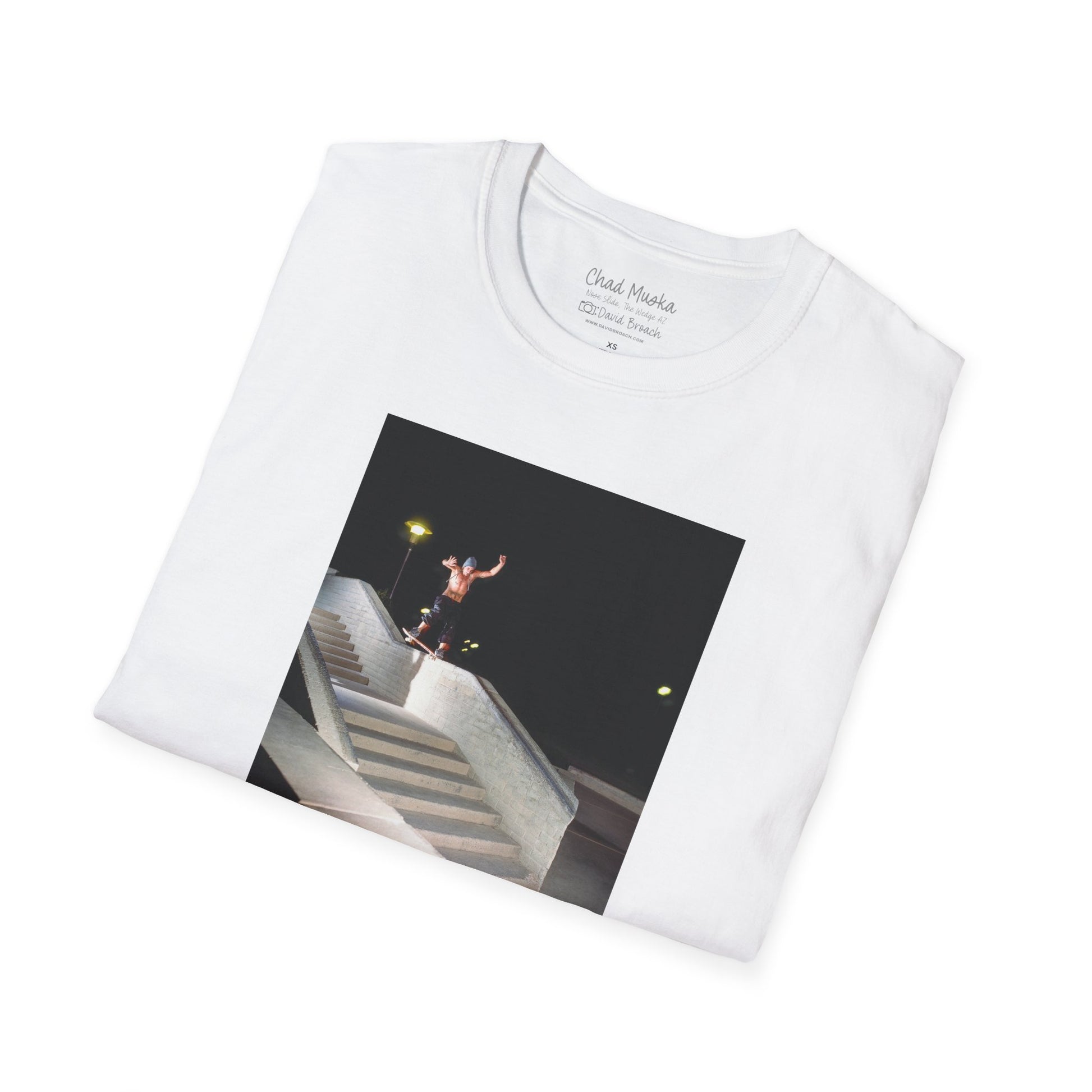 A neatly folded white crew neck short-sleeve T-shirt featuring a printed photo of A high-quality print featuring an iconic shot of Chad Muska in 1999 executing a smooth nose slide down the triple-kink Hubba rail at The Wedge in Phoenix, Arizona. Captured by photographer David Broach, this image showcases Muska’s signature style and fearless approach, making it a must-have for skateboarding enthusiasts and collectors."