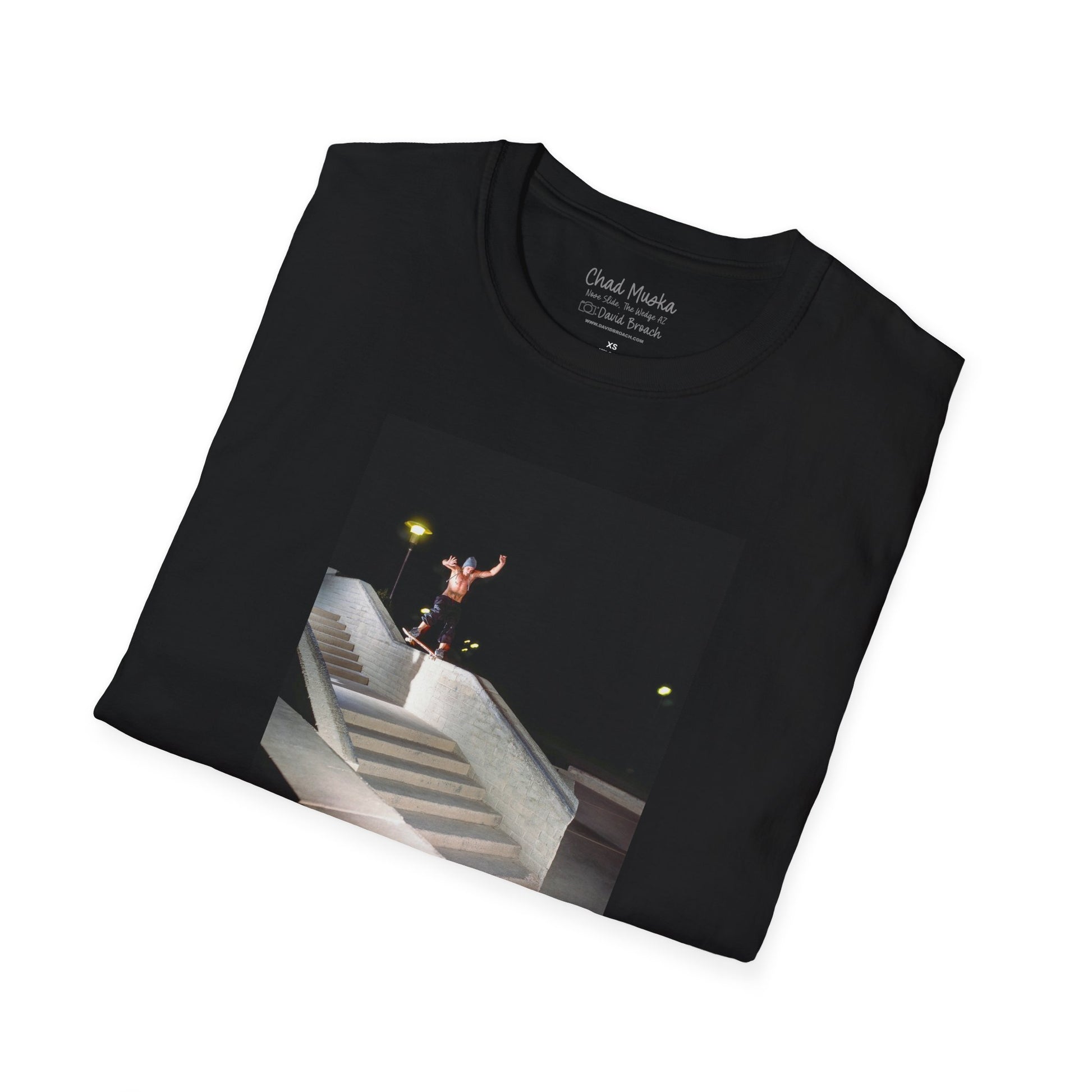 A neatly folded black crew neck short-sleeve T-shirt featuring a printed photo of A high-quality print featuring an iconic shot of Chad Muska in 1999 executing a smooth nose slide down the triple-kink Hubba rail at The Wedge in Phoenix, Arizona. Captured by photographer David Broach, this image showcases Muska’s signature style and fearless approach, making it a must-have for skateboarding enthusiasts and collectors."