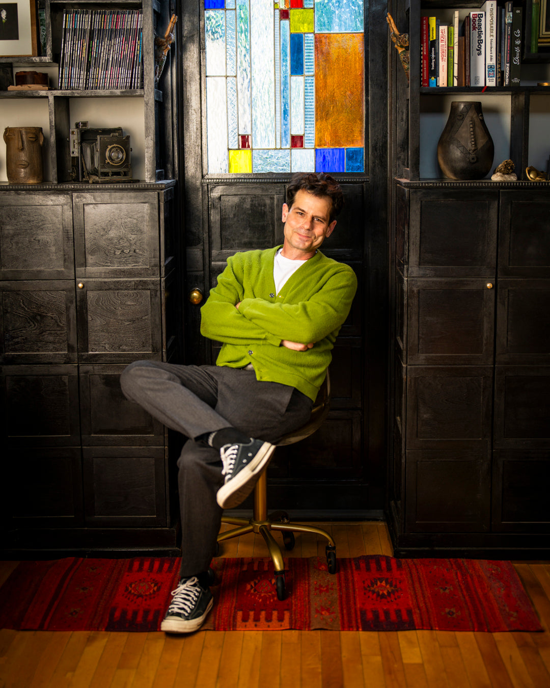 Portrait of David Broach sitting in desk chair in front f a stained glass window.